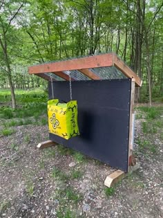 a small structure in the woods with a yellow bag hanging from it's side