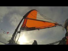 the man is flying his orange kite in the sky with sun shining through clouds behind him