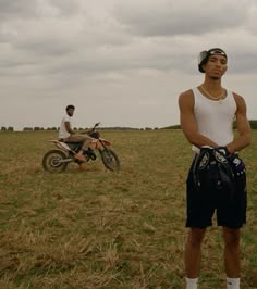 a man standing in a field next to a motorcycle