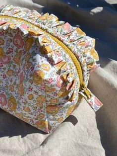 a floral print purse sitting on top of a white cloth covered bed sheet with yellow zippers