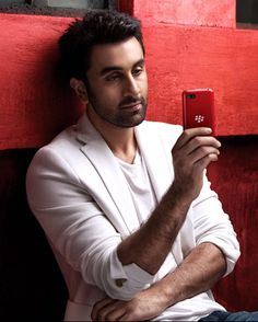 a man leaning against a red wall holding a cell phone