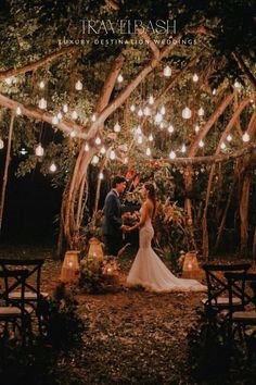 a bride and groom standing under a tree with lights hanging from it's branches