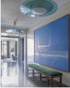 a large blue painting hanging on the wall next to a green bench in a hallway