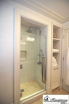 a walk in shower sitting inside of a bathroom next to a white robe hanging on the wall