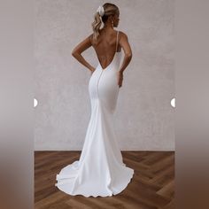 the back of a woman in a white dress standing on a wooden floor with her hands on her hips