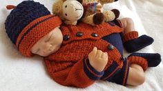 a baby laying on top of a bed next to two teddy bears wearing sweaters and hats