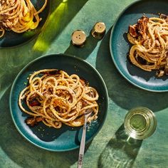 two plates with pasta and meat on them next to a bottle of wine, salt and pepper shakers