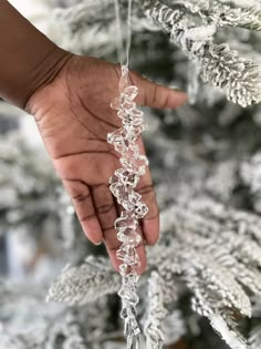 a hand holding an ornament hanging from a christmas tree with snow flakes on it