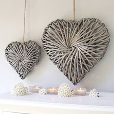 two wicker heart shaped wall hangings next to candles on a white table with flowers