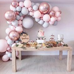 a table topped with lots of balloons next to a wall filled with cake and cupcakes