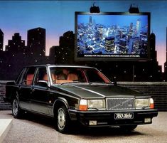 a black car is parked in front of a cityscape with a large screen