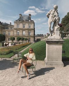 a woman sitting on a chair in front of a large building with a statue behind her