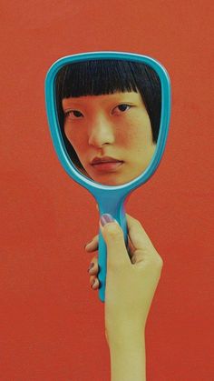 a woman holding a blue mirror in front of her face with the reflection of herself