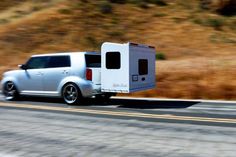 a silver minivan driving down the road next to a hill with brown grass on it