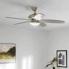 a ceiling fan in a white room with paintings on the wall