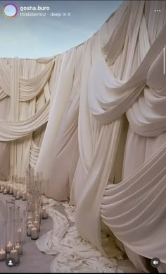 a room filled with lots of white candles and drapes on the wall next to each other