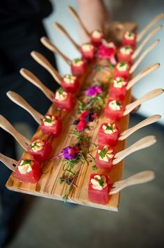 there are many small pieces of sushi on the wooden tray with utensils