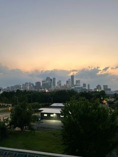 the city skyline is lit up at dusk with clouds in the sky and trees around it