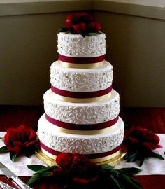 a three tiered wedding cake with red roses on the side and white frosting