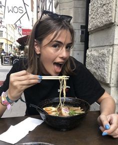 a woman holding chopsticks in her mouth while eating ramen from a bowl