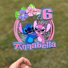 a hand holding up a pink and blue pin with the number six on it in front of a grassy area