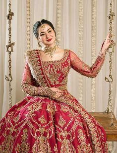 a woman in a red and gold dress sitting on a swing with her hands up