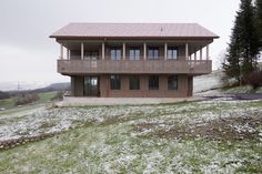 a house on top of a hill with snow on the ground and trees in the background