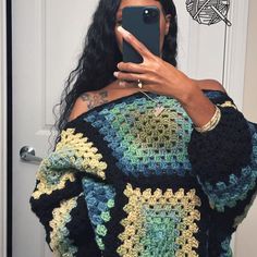 a woman taking a selfie in front of a door with her phone and crocheted granny shawl