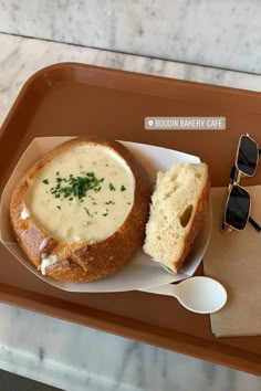 a bowl of soup and bread on a tray with some sunglasses next to it,