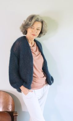 an older woman leaning against a wall wearing white pants and a blue knitted cardigan