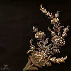 a gold and silver brooch with flowers on it's side, against a black background