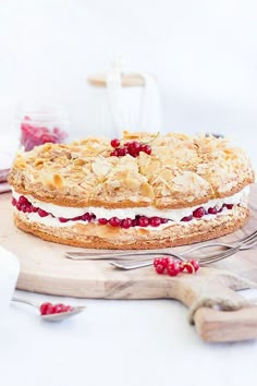 a cake with cranberry toppings on a wooden board next to silverware