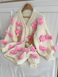 a knitted sweater with pink flowers on the front and back, sitting on a bed