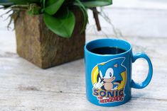 a blue sonic the hedge mug sitting next to a potted plant