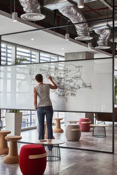 a man writing on a whiteboard in an office with lots of chairs and tables