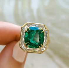 a close up of a person's hand holding a ring with an emerald and diamond in it