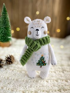 a white teddy bear with a green scarf and pine tree on it's chest