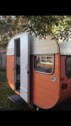 an orange and white camper parked in the grass next to a tree with its door open