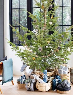 a small christmas tree in a basket next to a window with presents under it on the floor