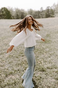 a woman with long hair is dancing in a field, wearing jeans and a white top