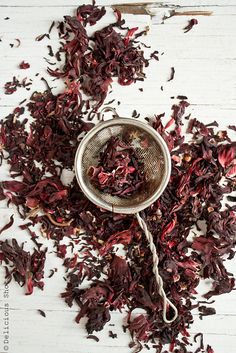 a strainer filled with dried red flowers on top of a white wooden tablecloth