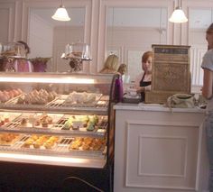 two women standing in front of a display case filled with pastries