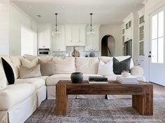 An extra large coffee table made with warm wood stands in front of a white corner sectional sofa with neutral pillows. It's accessorized by stacks of black and white books, a black ceramic pot, and a small white dish...   Image: houseofkeene