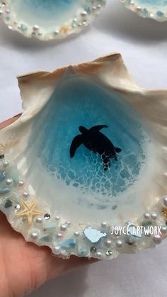 a hand holding an open shell with a sea turtle in it and pearls on the rim