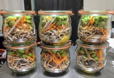 four glass jars filled with different types of vegetables and veggies on top of a table