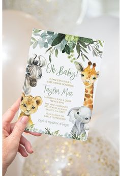 a person holding up a baby shower card with animals on it and greenery in the background