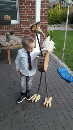 a little boy that is standing in front of a fake bird on a swing set