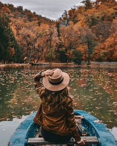 a woman sitting in a boat on top of a lake surrounded by fall colored trees