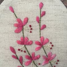 some pink flowers are on a white piece of cloth with red beads and thread in the middle