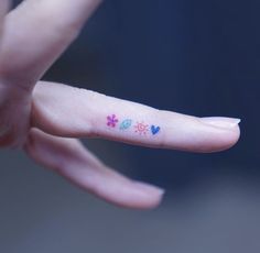 a person's finger with flowers and hearts tattooed on the tip of their thumb